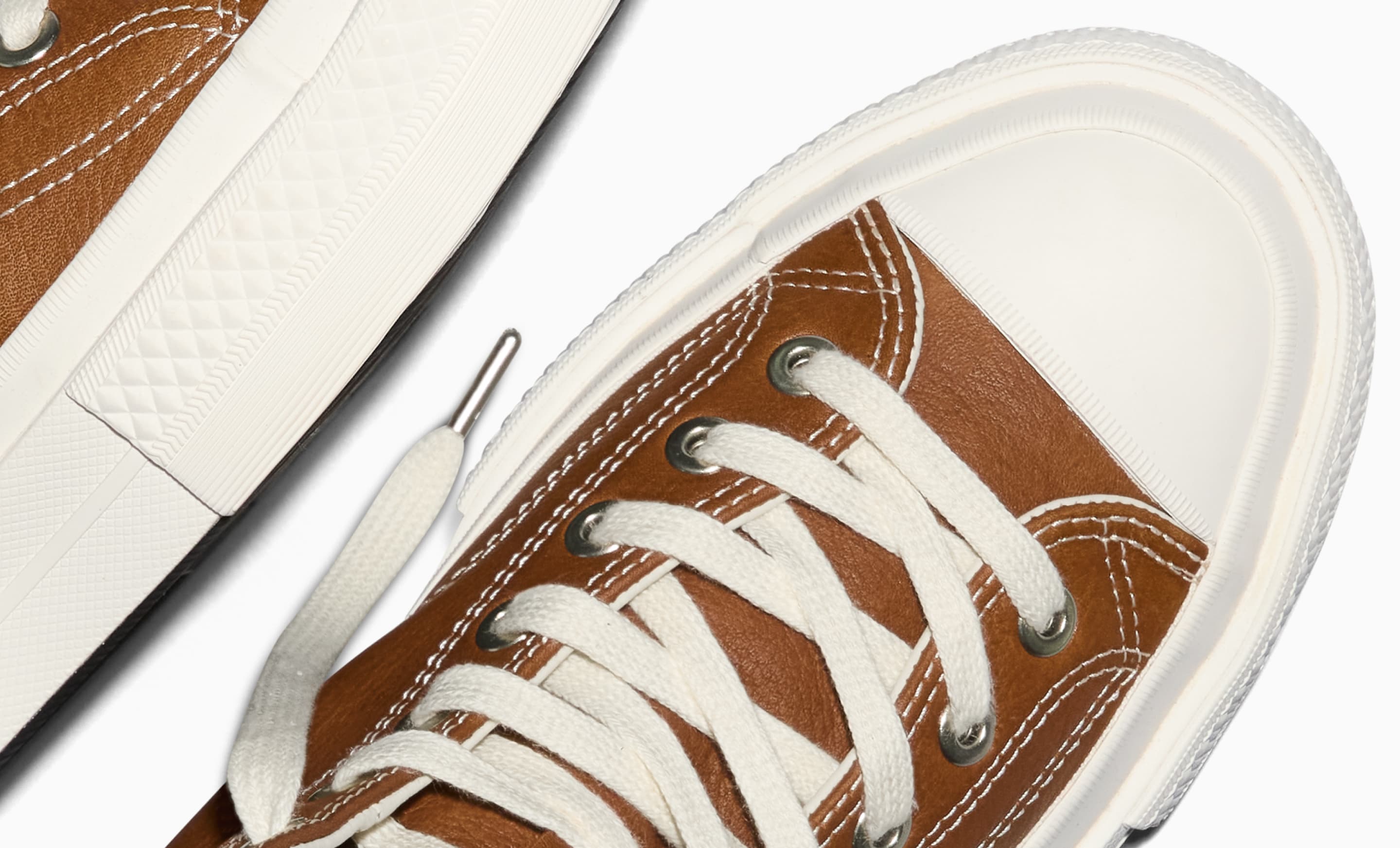 The image shows a close-up of a white sneaker with fabric laces threaded through metal eyelets. The shoe has detailed stitching and a textured rubber sole.