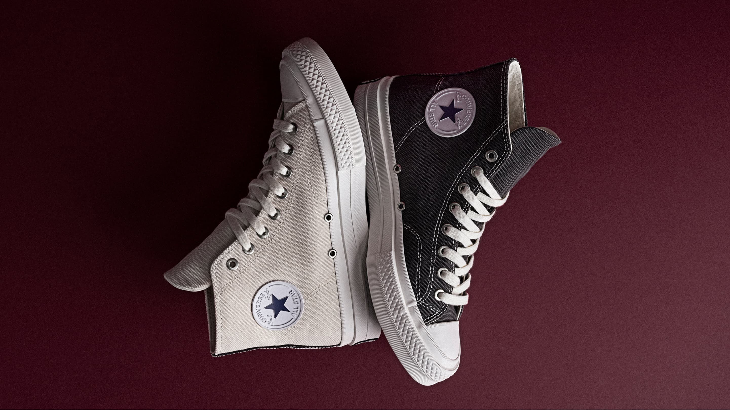 The image shows a pair of white Converse First String high-top sneakers placed on a black leather seat. One shoe is upright, displaying the embossed Converse logo, while the other lies flat, showing its black sole with a yellow Vibram label.