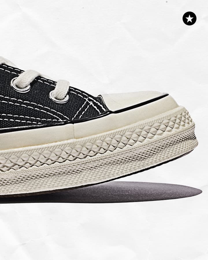The image shows a close-up side view of a black Converse Chuck Taylor All Star high-top sneaker. The shoe features the iconic circular patch on the ankle area, which includes a black star in the center and the text &ldquo;CONVERSE ALL STAR&rdquo; around it,