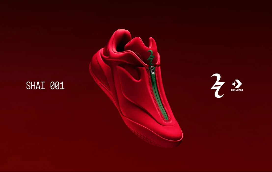 A vivid red sneaker with a central green zipper floats against a dark red background. The image shows the text “SHAI 001” on the left and a stylized emblem with the Converse star and wordmark on the right.
