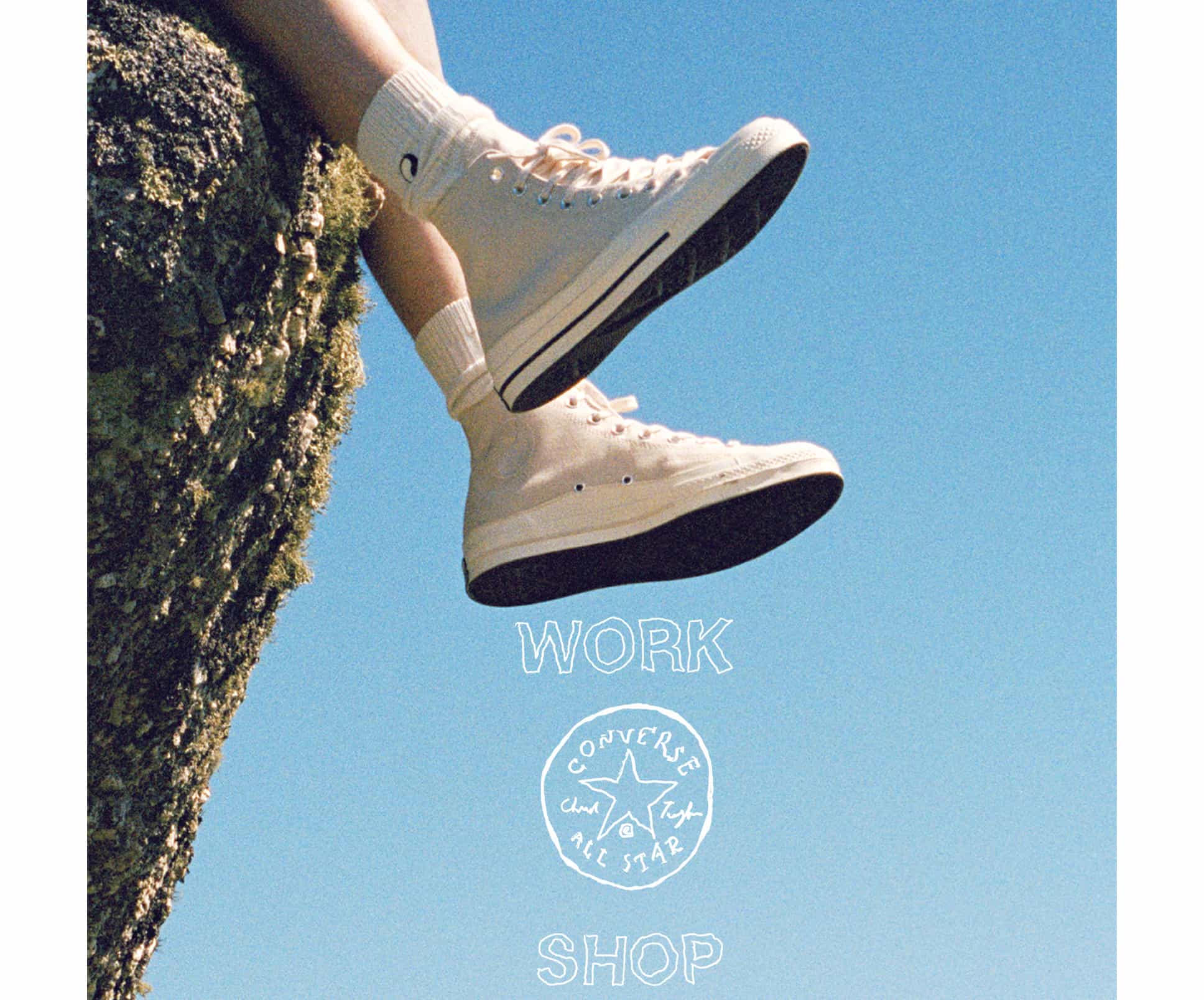 The image shows a person wearing white high-top Converse sneakers and white socks, sitting on the edge of a rocky surface against a clear blue sky. Below the shoes, the text “WORK SHOP” is displayed with the classic Converse All Star logo between the words