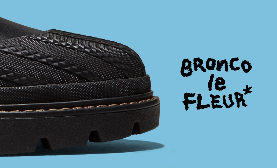 Close-up of the front portion of a black textured shoe and tread against a light blue background. To the right, black handwritten-style text reads 