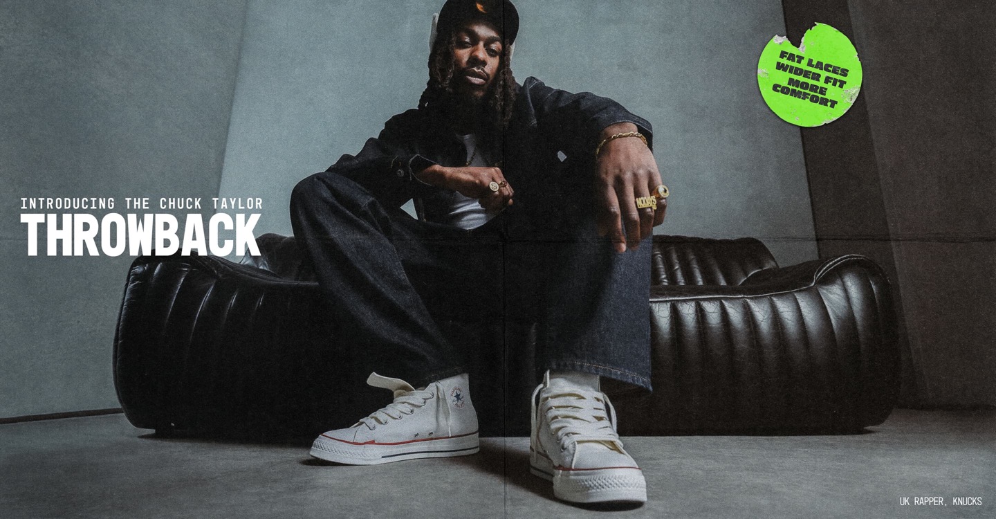 UK Rapper, Knucks, lounges on a black leather sofa, showing gold rings and a relaxed pose. The image includes a headline 