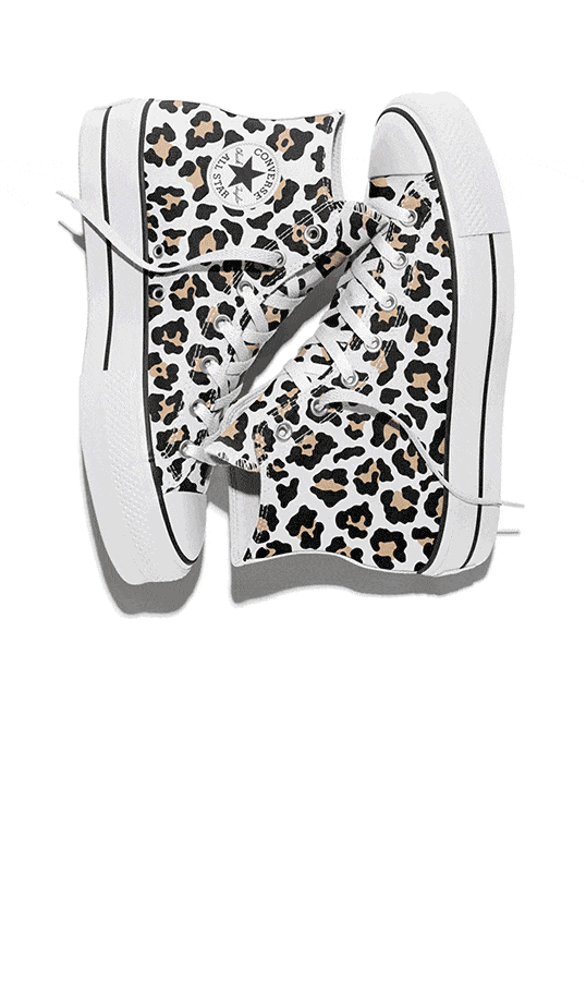 The image shows a pair of high-top Converse sneakers with a white base and a leopard print pattern in black and tan. The shoes have white laces, thick white soles with black stripes, and the classic Converse All Star logo on the side.