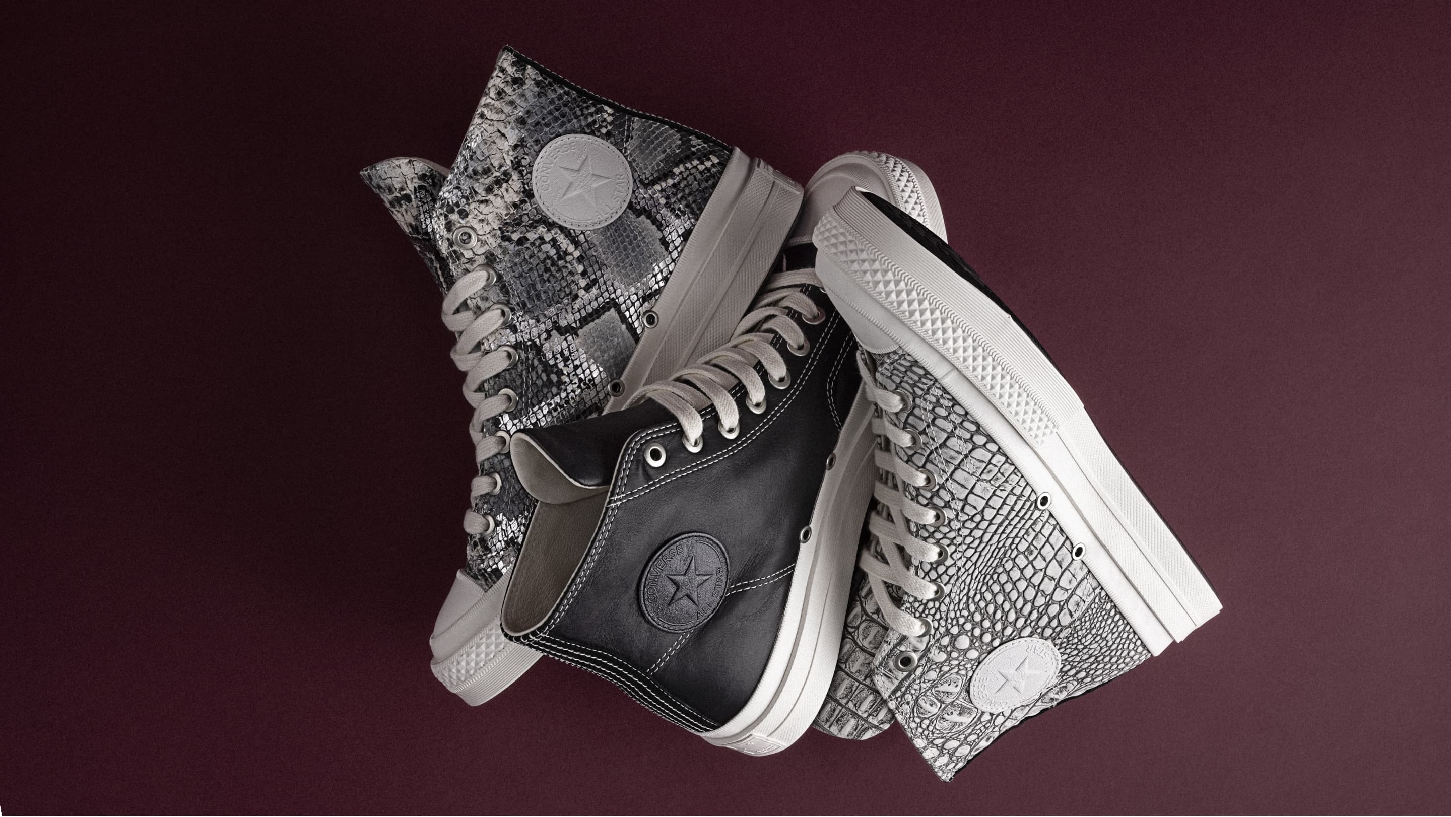 A moody close-up shows someone tying a Converse First String snake-print high-top sneaker with thick white platform soles and the Converse round ankle patch visible. 
