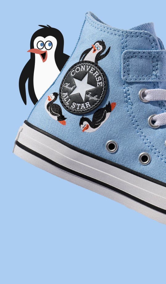 A light blue Converse Chuck Taylor high-top sneaker decorated with small penguin graphics and the circular &ldquo;CONVERSE ALL STAR&rdquo; logo patch. A large cartoon penguin with an open beak stands behind the shoe against a pale blue background.
