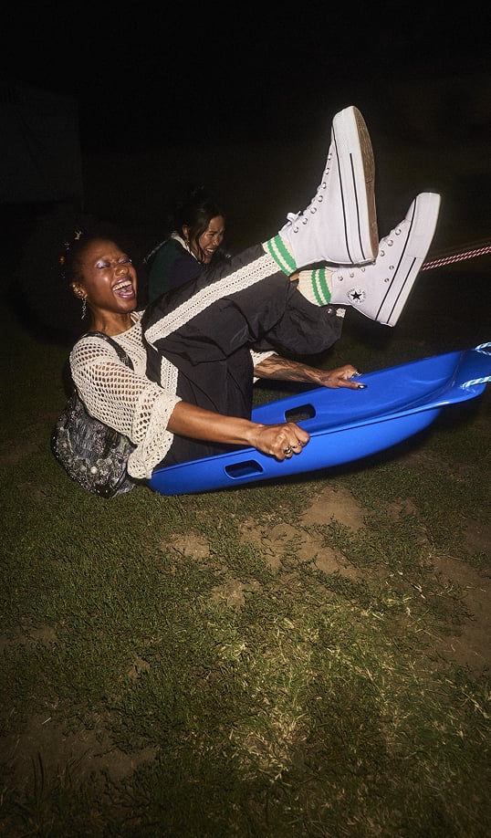 The image shows a person sitting on a sled smiling while wearing white high top Chuck Taylor All Star Lift Platforms. Overlaid text reads &rdquo;Chucks for the season. The shoes that start it all.&rdquo;