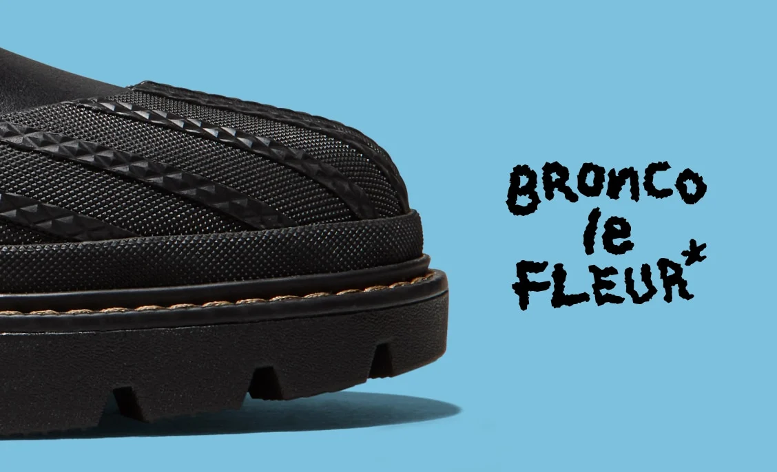 Close-up of the front portion of a black textured shoe and tread against a light blue background. To the right, black handwritten-style text reads 