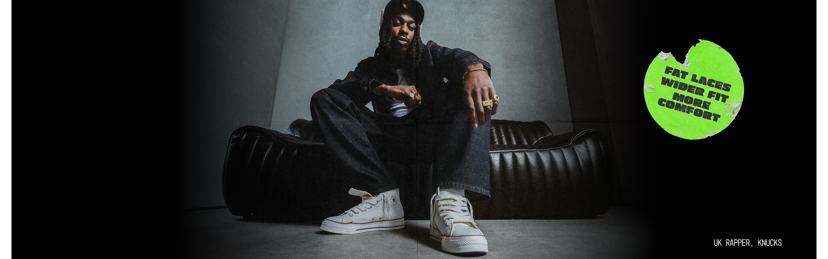 Photo of UK Rapper, Knucks, sitting on a leather couch wearing Chuck Taylor Throwback shoes