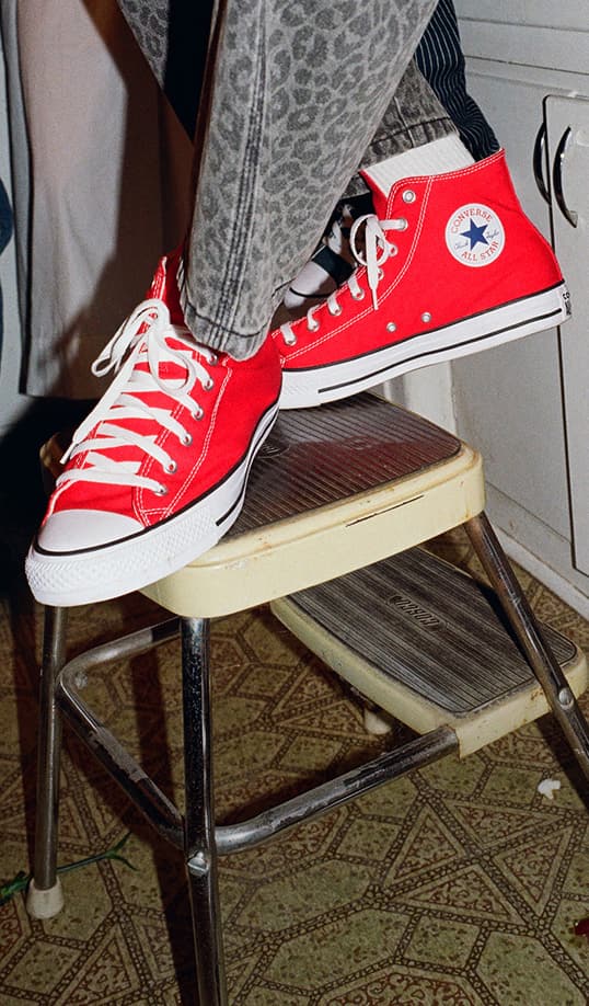 The image shows a person wearing bright red Converse Chuck Taylor All Star high-top sneakers with white laces and soles. 